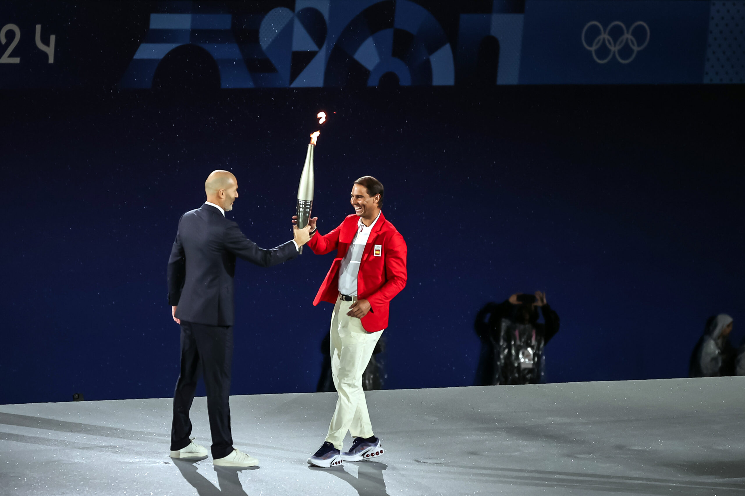 2024.07.26 - Jogos Olímpicos Paris 2024 - Cerimônia de Abertura. Rafael Nadal (de vermelho) e Zidane se encontram e trocam "de bastão" a tocha olímpica durante a Cerimônia de Abertura de Paris 2024. Foto: Gaspar Nóbrega/COB